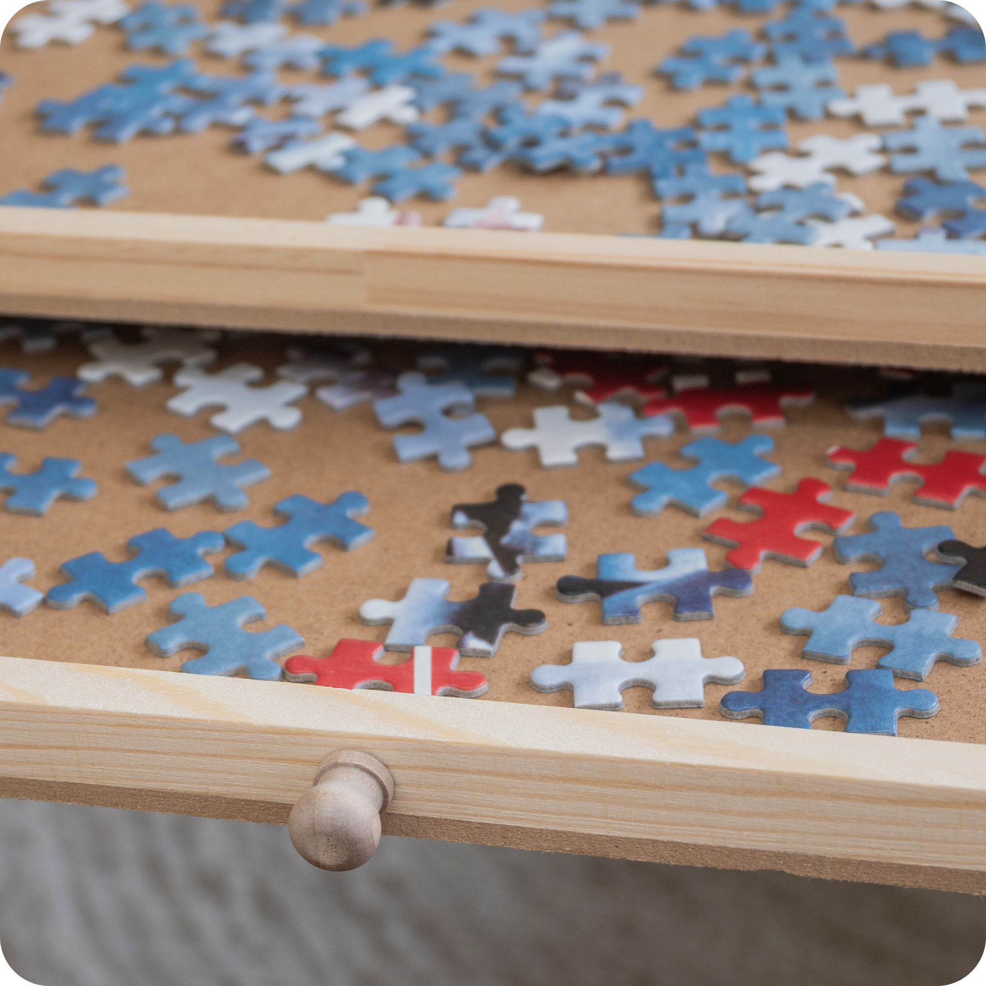 Een puzzeltafel gevuld met puzzelstukjes met een gedetailleerde focus op de uitgeschoven lade met opgeborgen puzzelstukjes.