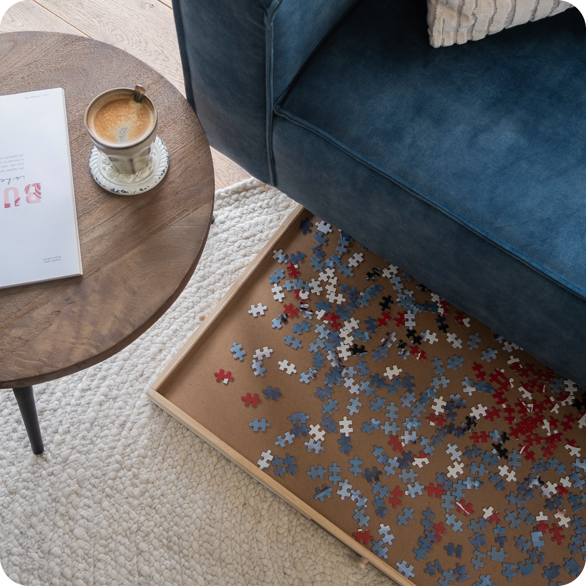 een bovenaanzicht van een blauwe bank met een puzzeltafel eronder. Deze puzzelplank wordt opgeborgen onder de bank.